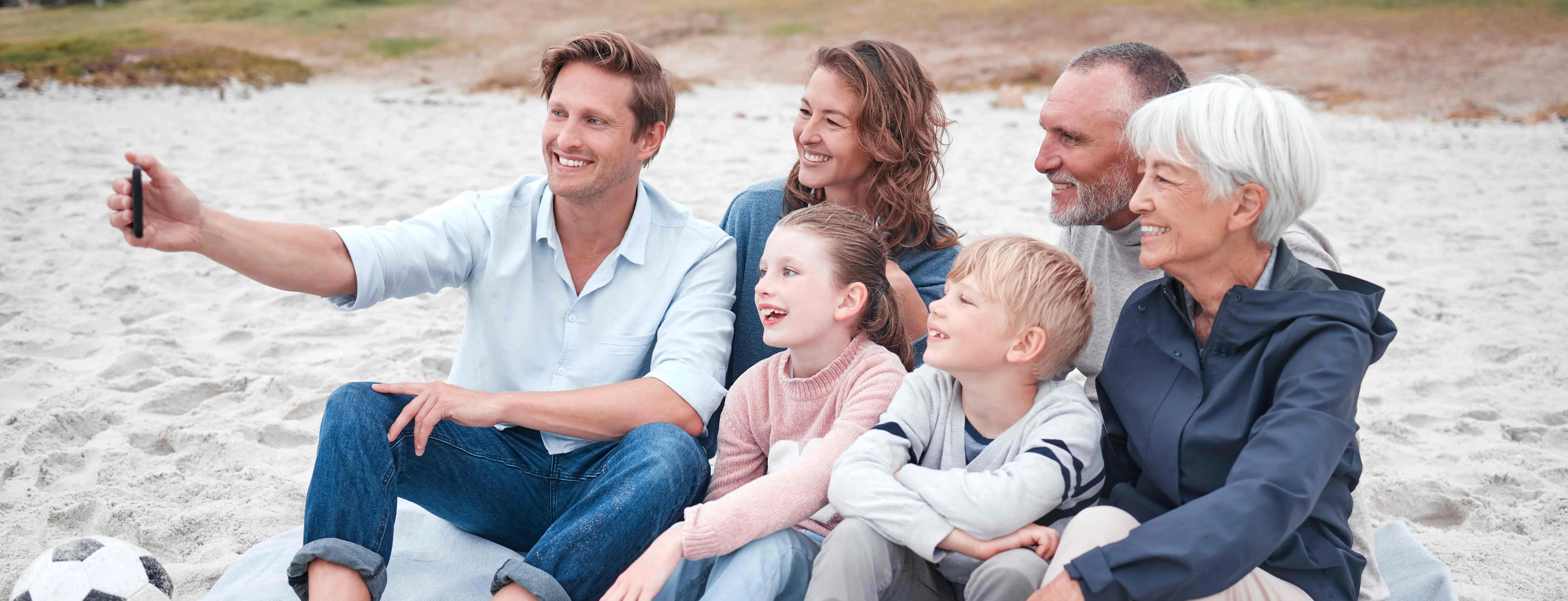 Family, selfie and beach with children, parents and grandparents taking a photograph while sitting on the sand.